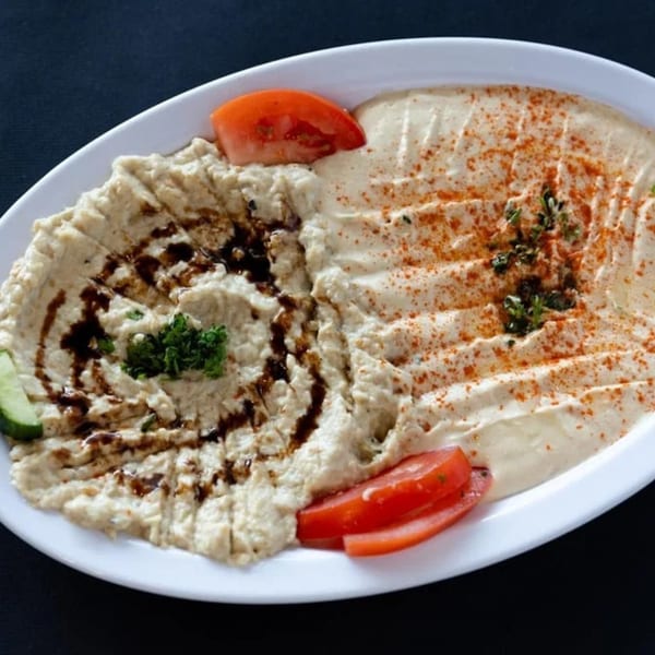 A white platter with two dips: baba ghanoush with balsamic glaze and hummus with paprika and herbs.
