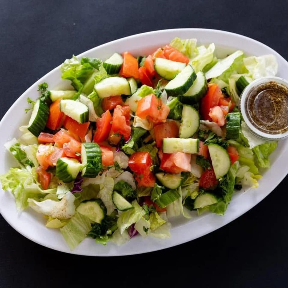 A fresh Sultan's Mediterranean salad with lettuce, cucumbers, and tomatoes, with dressing on the side.
