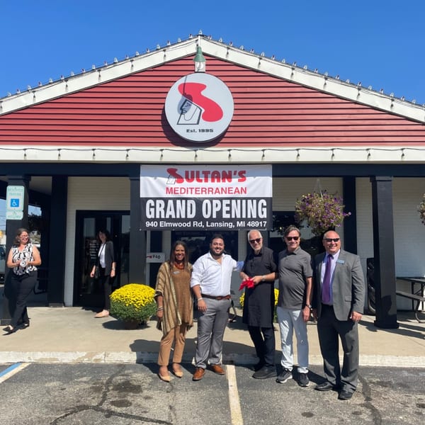 Five people stand outside Sultan's Mediterranean restaurant under a "Grand Opening" banner.