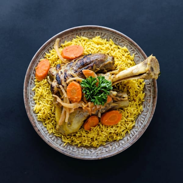 Lamb shank with yellow rice, carrots, onions, and parsley on a decorative plate.
