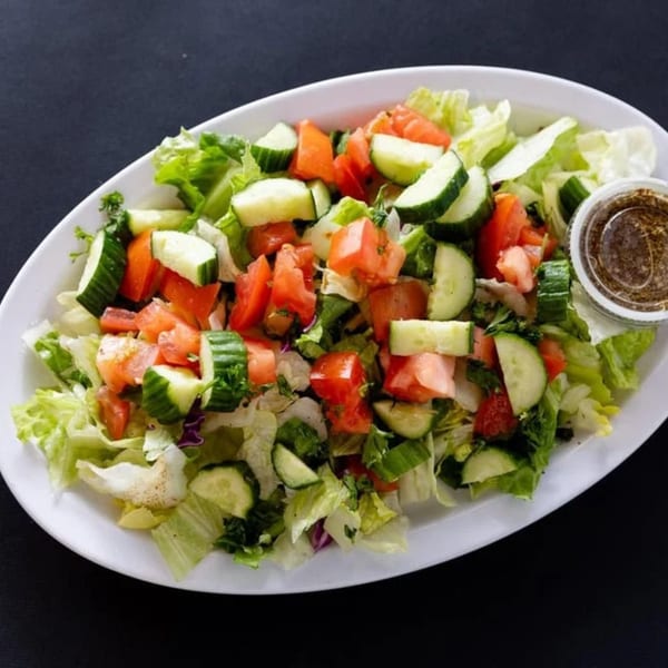 A fresh Sultan's Mediterranean salad with lettuce, cucumbers, and tomatoes, served with dressing.