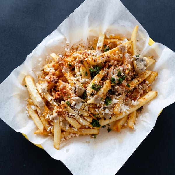 Golden french fries topped with white sauce, crumbled cheese, and spices in a paper-lined basket.