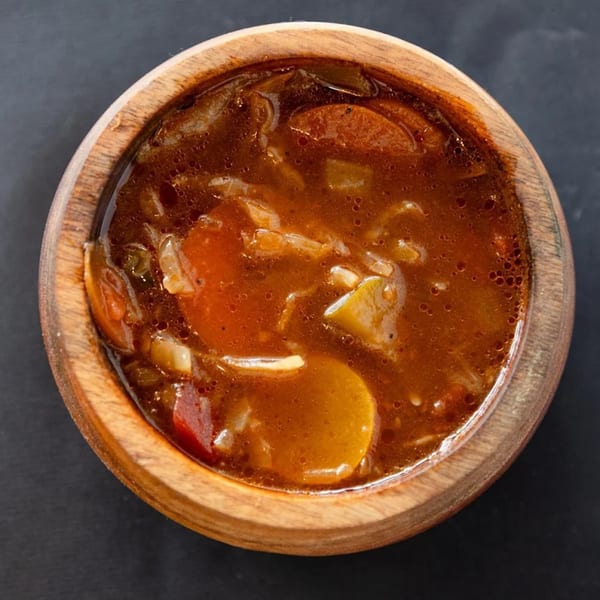 Overhead view of a wooden bowl filled with Sultan's hearty Mediterranean stew, featuring vegetables in a rich broth.