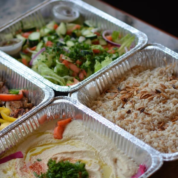 Mediterranean catering spread with salad, rice, hummus, and meat in foil containers.