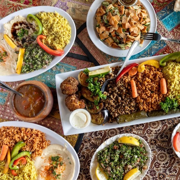 Overhead view of various Mediterranean dishes, including rice, hummus, salads, and falafel, on a patterned tablecloth.