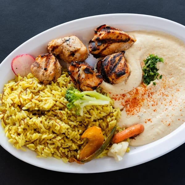 Grilled chicken pieces, yellow rice, hummus, and vegetables on a white plate from Sultan's Restaurant.