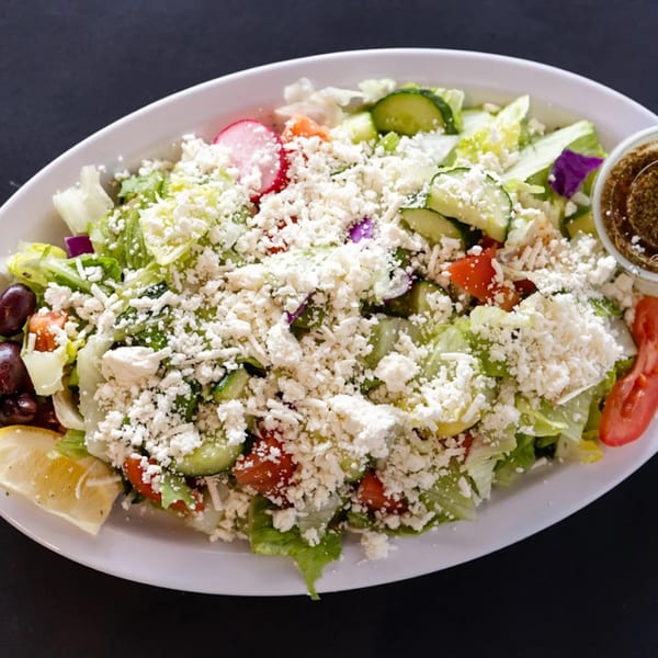 A vibrant Sultan's Mediterranean salad with lettuce, cucumbers, tomatoes, feta, olives, and a lemon wedge.