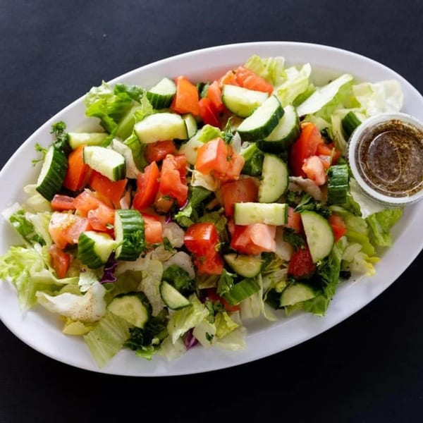 A fresh Mediterranean salad with lettuce, cucumbers, and tomatoes, served with dressing on the side.