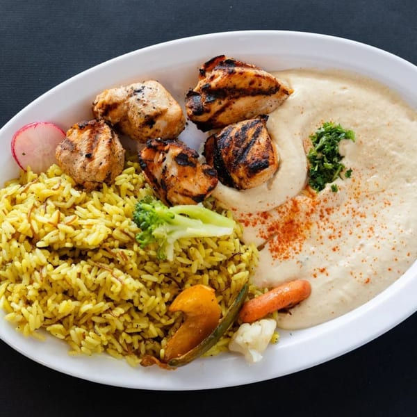 Sultan's Restaurant's grilled chicken with yellow rice, hummus, and mixed vegetables on a white plate.