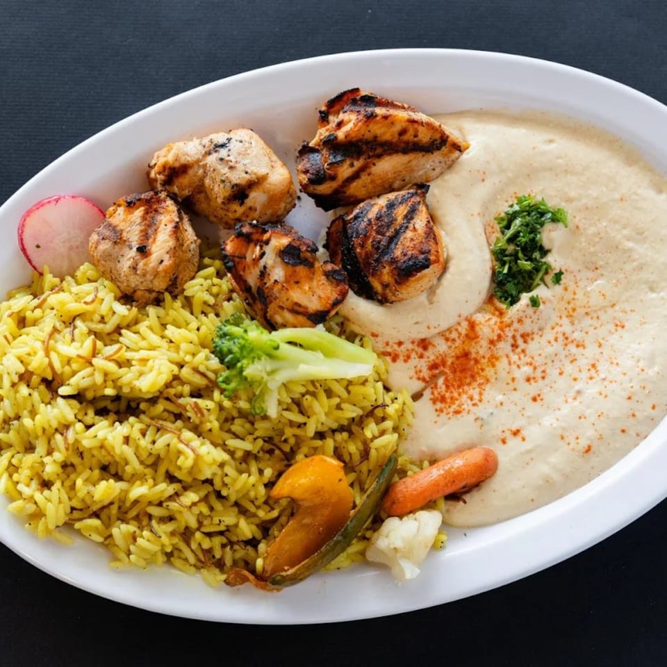 Sultan's Restaurant's grilled chicken with yellow rice, hummus, and mixed vegetables on a white plate.
