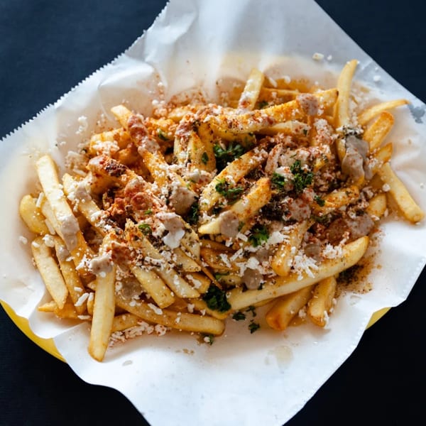 Sultan's Restaurant's Mediterranean fries, topped with feta cheese, sauce, and spices, served in a basket.